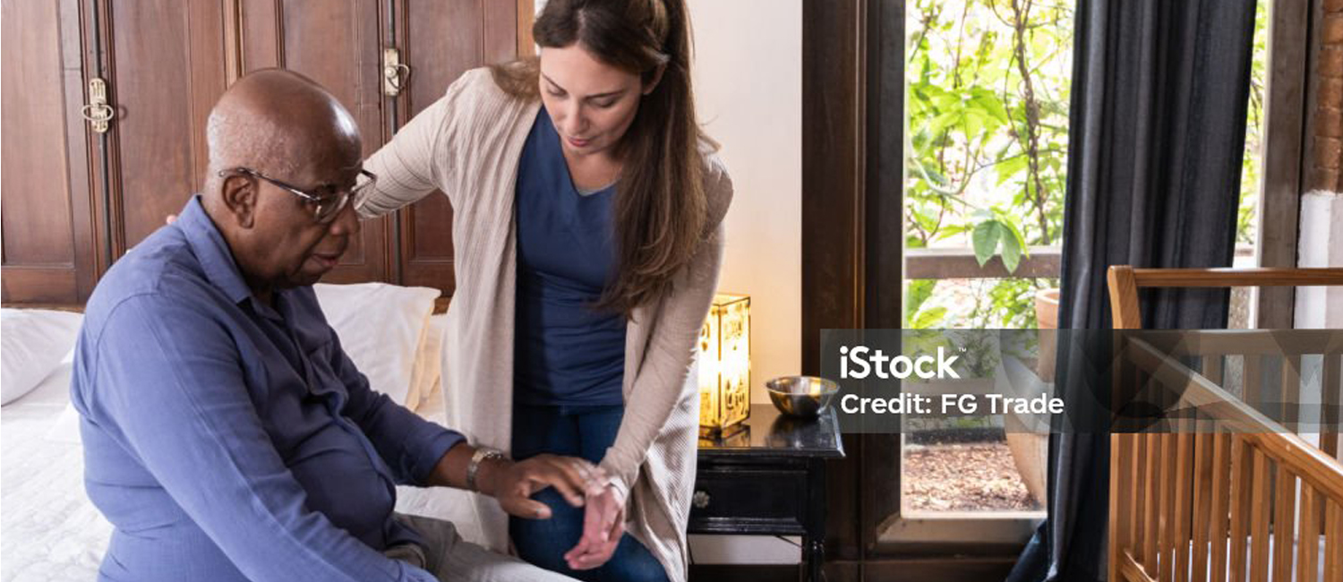 aide helping senior man from bed